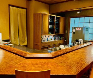 L-shaped wooden counter and seating at Ryutakuzenji 宿坊 in Gunma with shoji screens and shelving