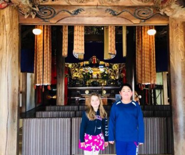Two visitors on tatami near ornate altar inside Ryutakuzenji temple lodging, Gunma