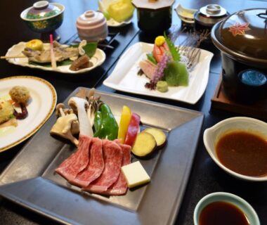 Multi-course Japanese meal with sashimi, raw sliced beef and dipping sauces on a ryokan dining table