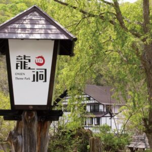 Wooden lantern sign with Japanese characters beside Ryuudo ryokan building amid verdant trees in Gunma