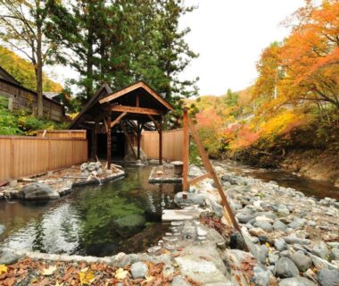 Wooden riverside onsen bath beside rocky stream with autumn maples at Ryuudo, Gunma, Kanto