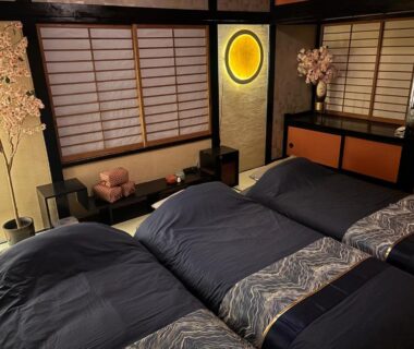 Three futon beds in tatami room with shoji screens, decorative blossoms, low table, and warm lighting at SAKURA inn