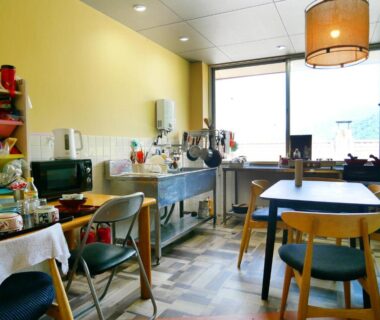 Small communal dining and kitchenette at SDGs BASE AQUA PLUS in Ishikawa, rustic chairs and pendant light