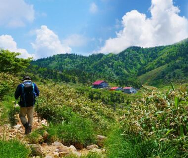 Traveler on grassy mountain path approaching SDGs BASE AQUA PLUS in Ishikawa
