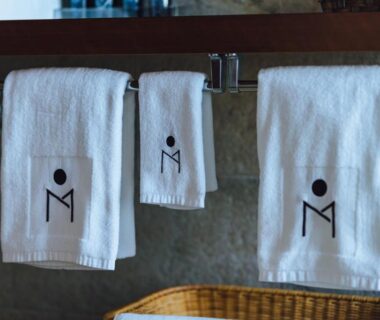 Three white towels with logo hanging on rail above wicker basket at SEKIYA RESORT Terrace Midoubaru bathroom
