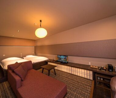 Warm lit guest room with twin beds, chaise lounge, low table and media cabinet at SEKIYA RESORT in Ōita