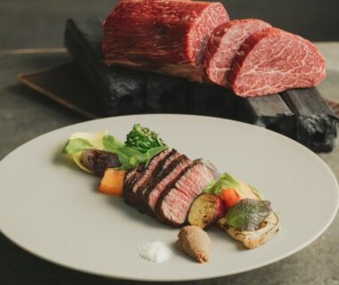 Sliced seared beef with roasted vegetables on white plate and raw beef slab on board in background