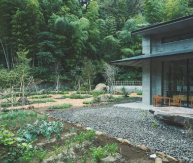 Wooden veranda and chairs beside gravel courtyard and vegetable beds with bamboo grove backdrop at SOKI ATAMI, Shizuoka
