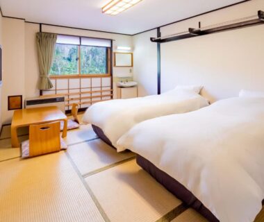 Tatami room with twin beds, low table and window view of trees in Nagano