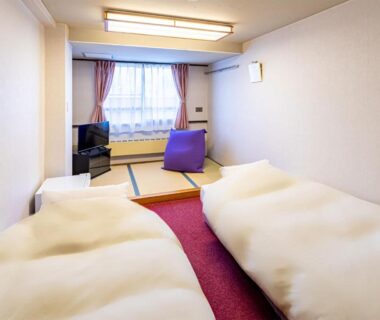 Bright guest room with two futon beds, raised tatami seating area and window view at Sachinoyu Hotel Shiga Kogen, Nagano