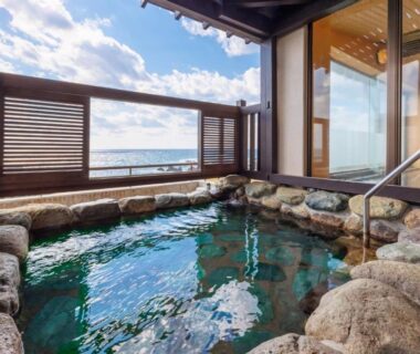 Stone-lined onsen bath with sea view through wooden shutters at Sado Resort Hotel Azuma in Niigata