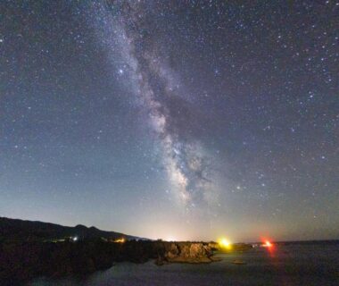 Milky Way above coastal shoreline with distant lights near Sado Ryosou Minato, Niigata