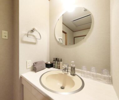 Bathroom vanity with round mirror, toiletries, cups and hand towel at Saga Fuga ryokan in Saga, Japan