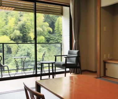 Tatami seating area with low table, chairs and balcony overlooking lush bamboo forest at Saga Fuga in Saga