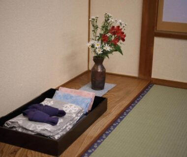 Folded bedding and robes on a tray beside tatami mats and a floral arrangement in a Kyoto ryokan room