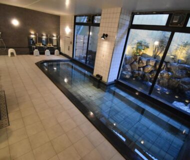 Large indoor tiled communal bath with shower stools and windows overlooking rock garden at Saga Grace Hotel Kyoto