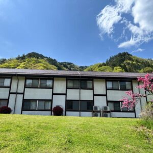 Low hillside view of Sagirisou ryokan facade, grassy lawn and flowering tree in Nagano, Chūbu region