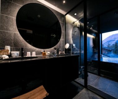 Dark stone bathroom with round mirror and glass bathing area at Saigakukan in Oita, Kyushu