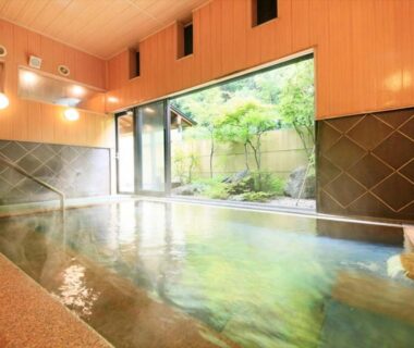 Wood-lined indoor onsen with large window and garden view at Saikatei Jidaiya, Yamagata
