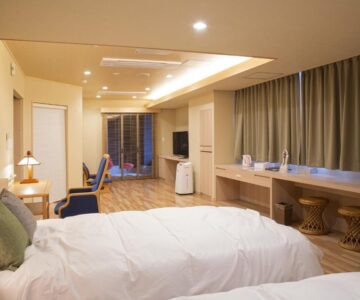 Spacious twin room with two beds, long desk, stools, and sliding glass door at Sakaeya Hotel Yamagata