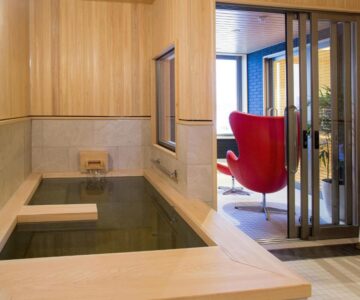 Indoor wooden bath next to modern lounge chair at Sakaeya Hotel, Yamagata, Japan