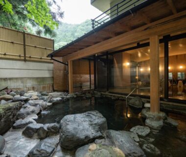Stone-lined onsen beside wooden pavilion and mountain foliage at Sakahijiri Nikko, Tochigi