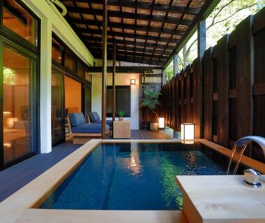 Covered rectangular onsen bath on wooden deck with sliding glass doors and lanterns at Sakahijiri gyokushoen Shizuoka