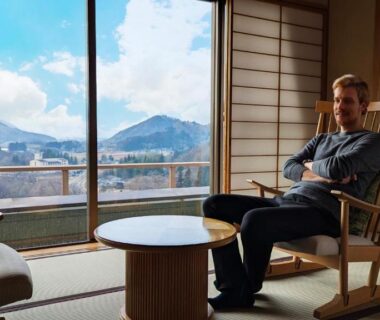 Man seated in tatami room with low table and mountain view through a large window at Sakan, Miyagi
