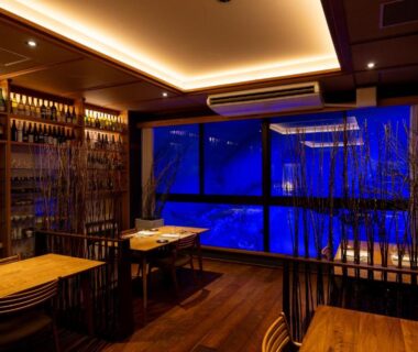 Wooden dining area with sake bottle shelves and blue-lit window at Sake Hotel Tamakiya, Niigata