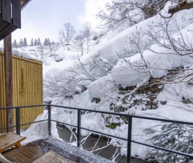 Balcony with wooden chairs and railing overlooking snow-covered hillside at Sake Hotel Tamakiya in Niigata Chūbu