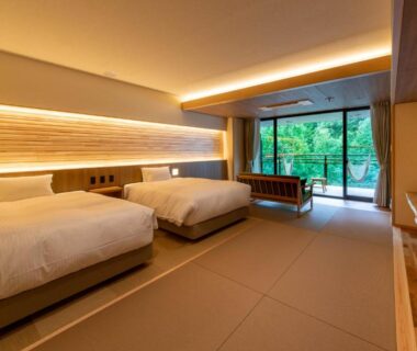 Spacious tatami-floored twin room with low beds and balcony overlooking lush greenery at Sakunami Onsen Yuzukushi Salon Ichinobo, Miyagi