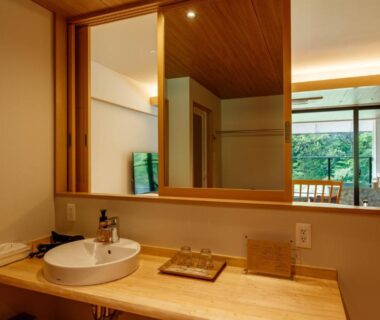 Wooden vanity with round sink and large mirror overlooking a tatami room at Sakunami Onsen Yuzukushi Salon Ichinobo, Miyagi