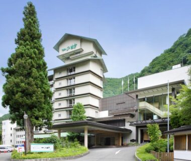Multi-story ryokan exterior with entrance canopy and mountain backdrop at Sakunami Onsen Yuzukushi Salon Ichinobo, Miyagi