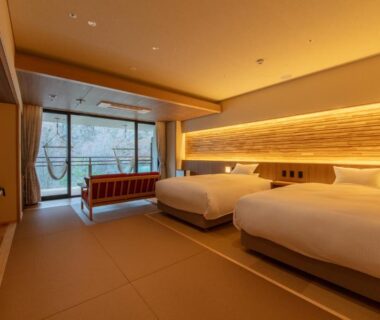 Japanese-style room with tatami flooring, twin beds and large window overlooking trees at Sakunami Onsen Ichinobo in Miyagi