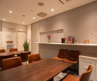 Communal dining area with wooden tables, brown chairs and serving counter at Sakura Ryokan Asakusa Iriya, Tokyo