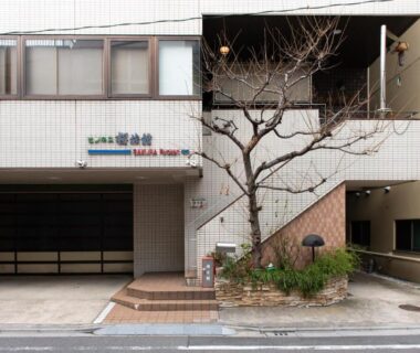 Tiled building entrance with small tree and signage for Sakura Ryokan Asakusa Iriya in Tokyo