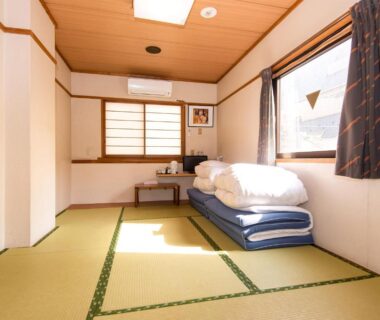 Sunlit tatami room with stacked futon, shoji window and low table at Sakura Ryokan Asakusa, Tokyo