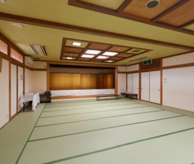 Spacious tatami hall with shoji doors, wooden ceiling panels and a low stage at Sakura no Yakata, Yamanashi