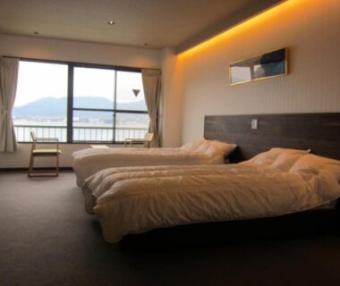 Spacious twin bedroom at Sakuraya with large window overlooking waterfront and distant hills in Hiroshima