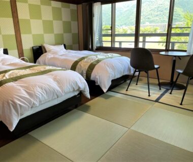 Tatami-floored room with three beds, table and chairs, balcony showing green hillside view at Sanso Tanaka, Oita