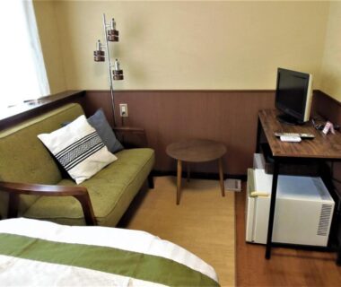 Bed corner with green throw, sofa and desk at Sanso Tanaka in Ōita, Kyūshū