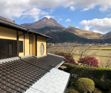 Tiled ryokan roof and veranda overlooking fields, garden shrubs and distant mountains in Oita