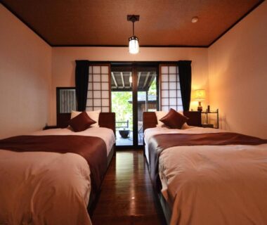 Twin beds in serene room with shoji screens, wooden floor and sliding doors opening to veranda with greenery