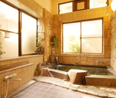 Stone-lined indoor bathing area with wooden accents, tiled floor and frosted windows at Sansou Nagisa, Kanagawa