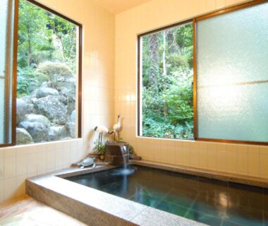 Tiled indoor onsen bath with windows overlooking lush garden at Sansou Nagisa in Kanagawa
