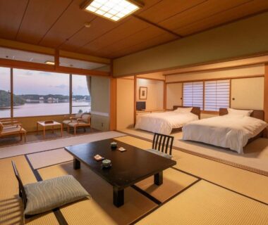 Tatami room with twin beds, low table and shoji screens overlooking a coastal bay at Sansuikan Kinryu, Shizuoka