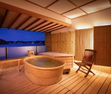 Wooden soaking tub on deck overlooking water with bamboo screens and wooden chair at Sansuikan Kinryu, Shizuoka