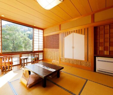 Sunlit tatami room with low table, wooden floor chairs, shoji screens and large window framing lush greenery at Sansuisou, Kanagawa