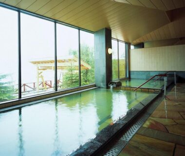 Indoor onsen bath with floor-to-ceiling windows and stone floor at Marukoma Onsen Ryokan, Hokkaidō