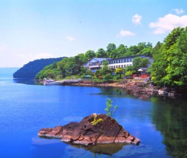 Tree-lined rocky coastline with small islet beside Marukoma Onsen Ryokan in Hokkaidō Japan
